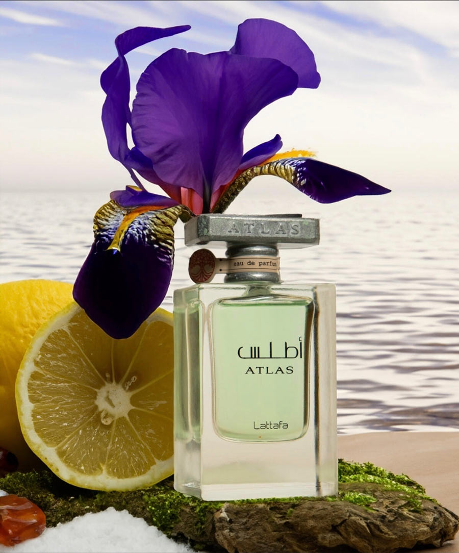 Lattafa Atlas perfume bottle surrounded by a sliced lemon, iris flower, and ocean background.